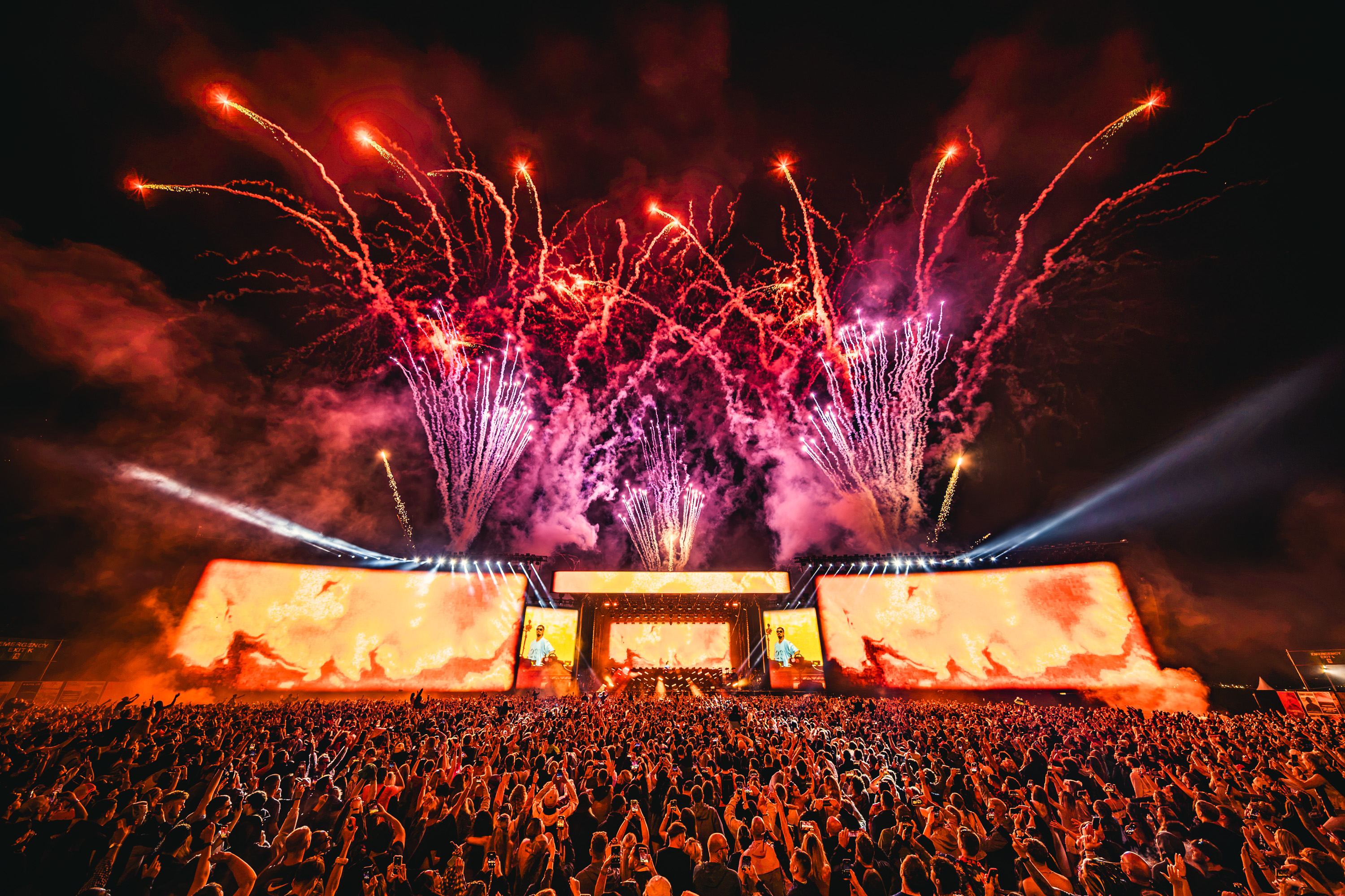 Fireworks erupt above the Arc Stage at Pepsi MAX presents Creamfields as a large crowd watches beneath orange LED screens and stage lighting.