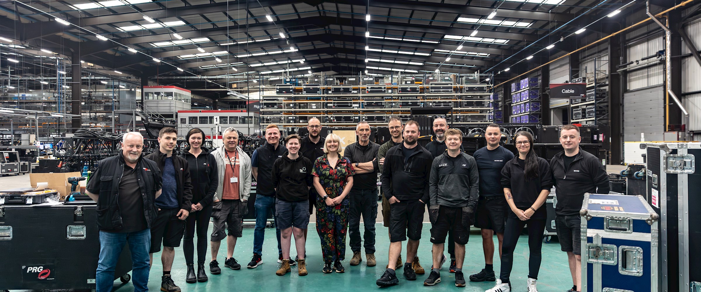 Crew members from Moulin Rouge! World Tour, Les Misérables: The Arena Spectacular and Jersey Boys pose together inside PRG's Longbridge facility, standing among staging, lighting and touring equipment ahead of upcoming tour preparations and reprep work.